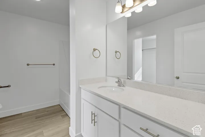 Bathroom featuring a white vanity with an integrated sink, broad wall mirror, and wood-finish flooring