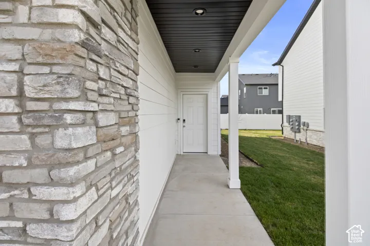 Stone facade detailing, covered entry, concrete walkway, recessed lighting, and white siding