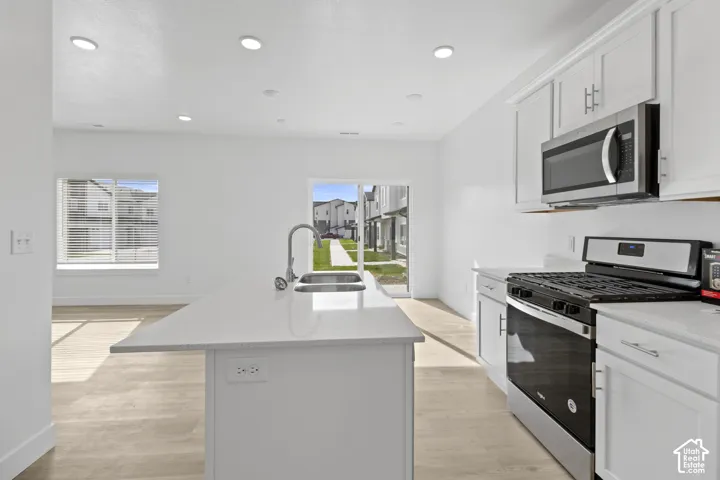 Modern kitchen featuring a kitchen island with sink, stainless steel appliances, white cabinetry, and recessed lighting