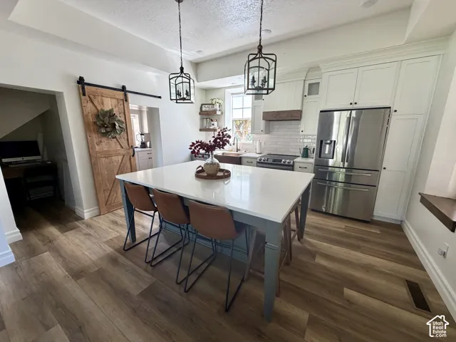 Open-concept kitchen featuring an oversized island with seating, stainless steel appliances, white subway tile backsplash, and wood-finish flooring