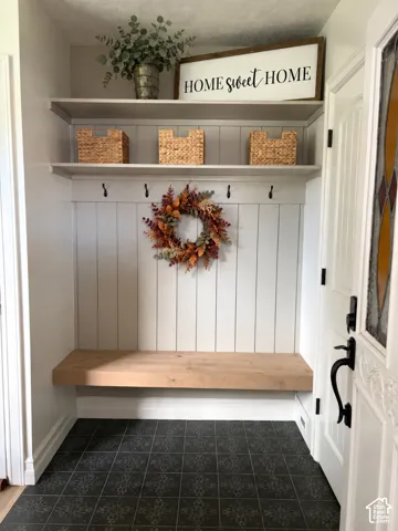 Built-in entryway bench with white shiplap-style wall paneling, integrated shelving, and dark patterned floor tiles