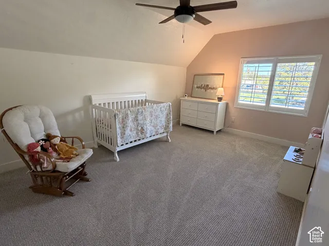 Bright and spacious nursery featuring vaulted ceilings, ceiling fan with integrated lighting, and abundant natural light from dual windows with plantation shutters