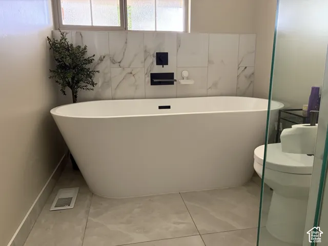 Freestanding soaking tub with matte black fixtures, marble-look tile surround, and light-toned floor tiling