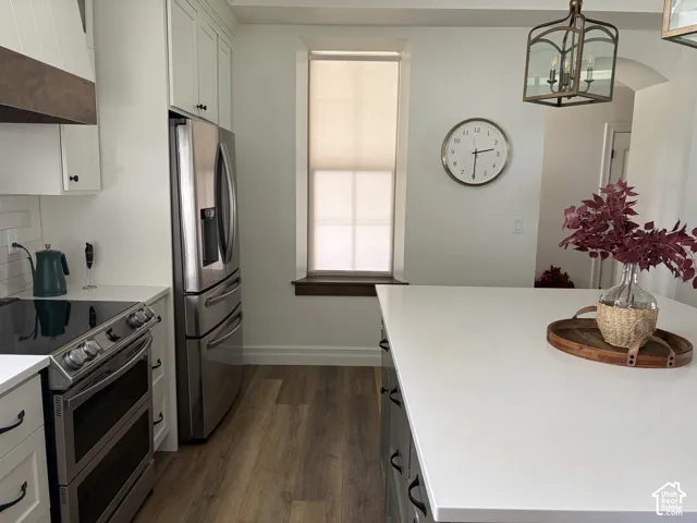 Kitchen featuring wood-finish flooring, white cabinetry, stainless steel appliances, a white solid surface countertop, and a built-in oven range