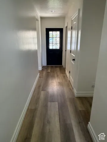 Wood-finish flooring with white baseboards, recessed ceiling lighting, and a dark-paneled door with transom-style window