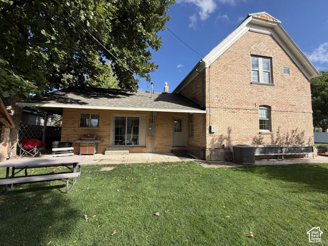 Brick exterior with a covered patio, expansive lawn, sliding glass door, and multiple windows