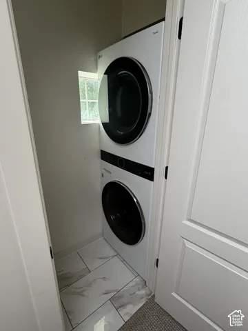 Upstairs laundry: White stacked laundry appliances, window, and tile flooring