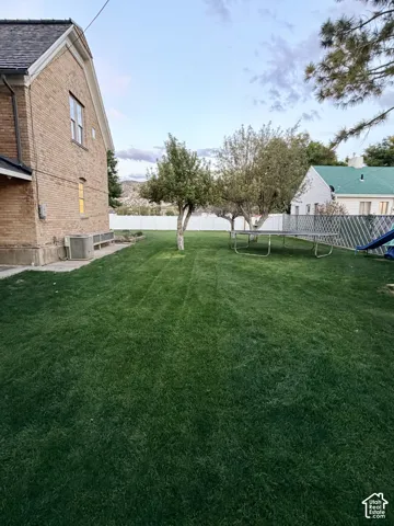 Expansive lawn area with mature trees, a durable privacy fence, and a brick exterior structure