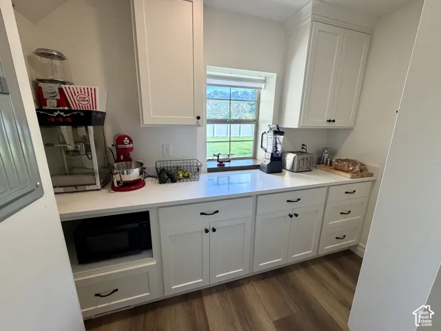 White shaker-style cabinetry with black hardware, white countertops, wood-finish flooring, and a built-in microwave niche