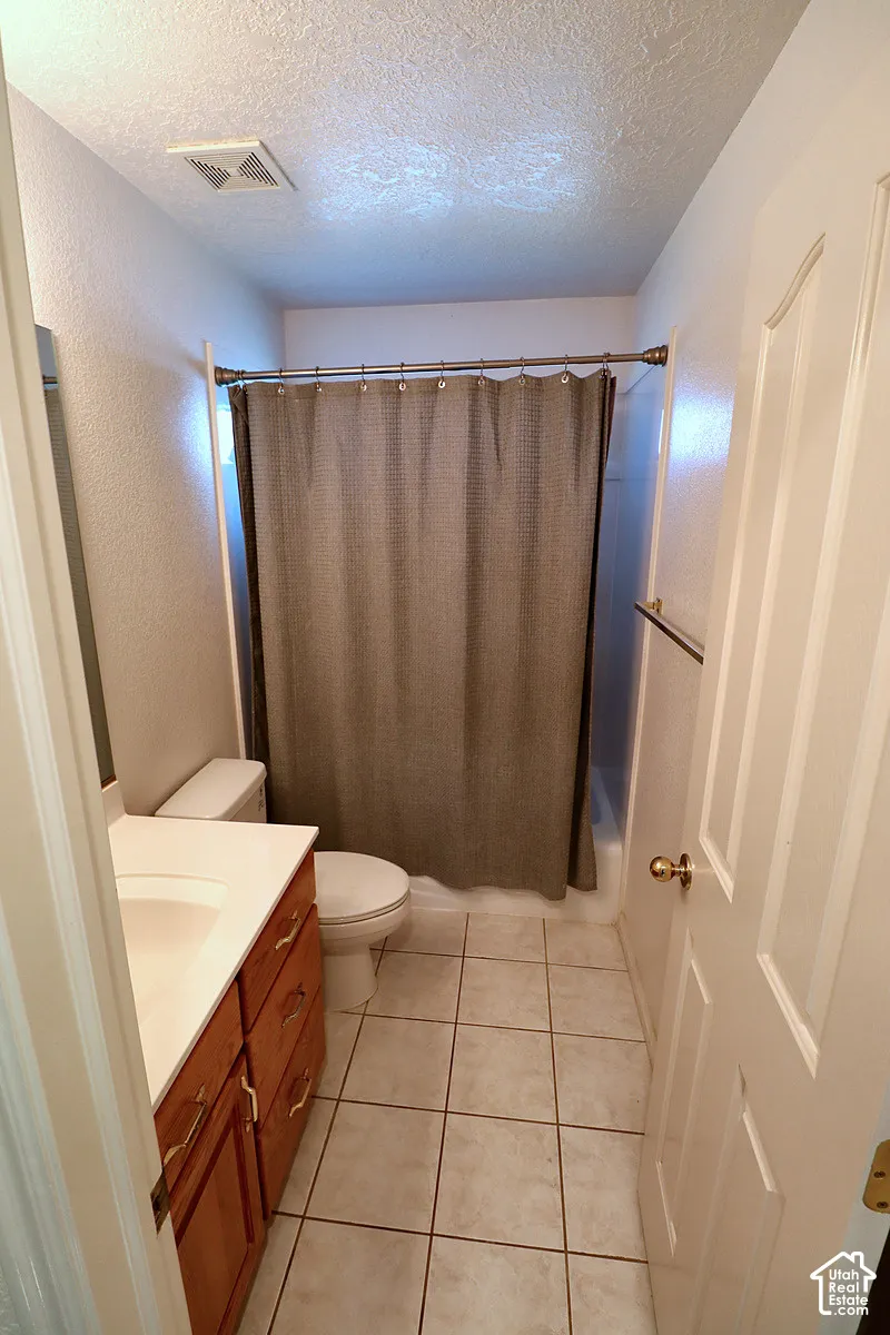 White tile flooring, wood-finish vanity with white countertop, and a white toilet