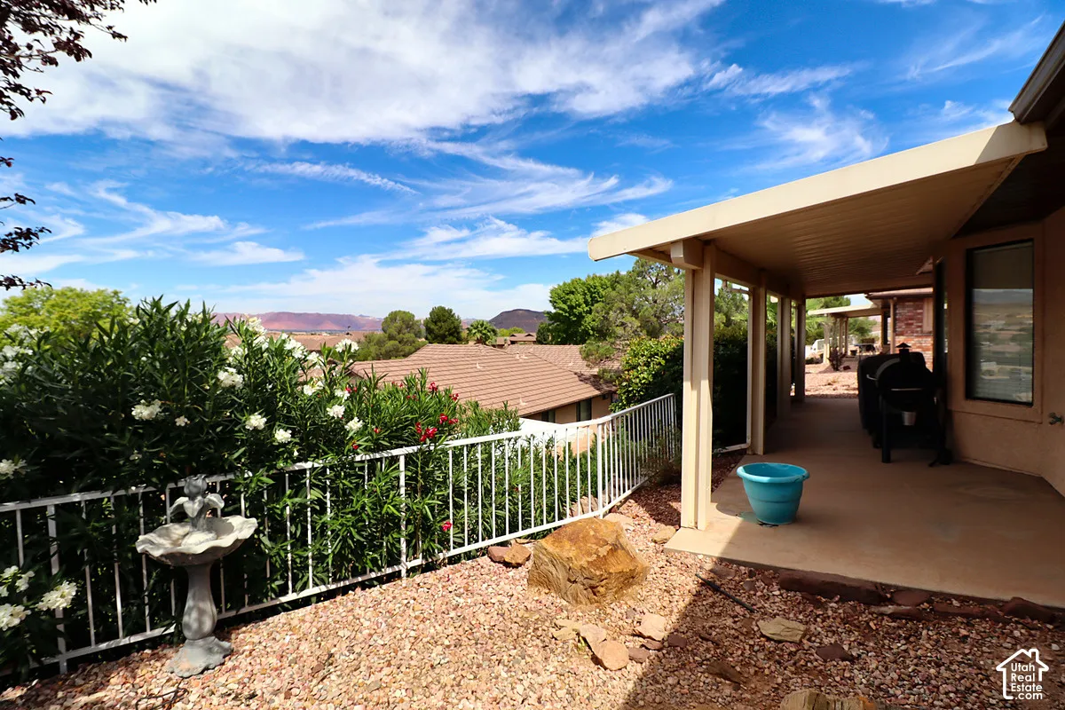 Expansive covered patio with a concrete surface, bordered by a white metal fence and varied mature landscaping