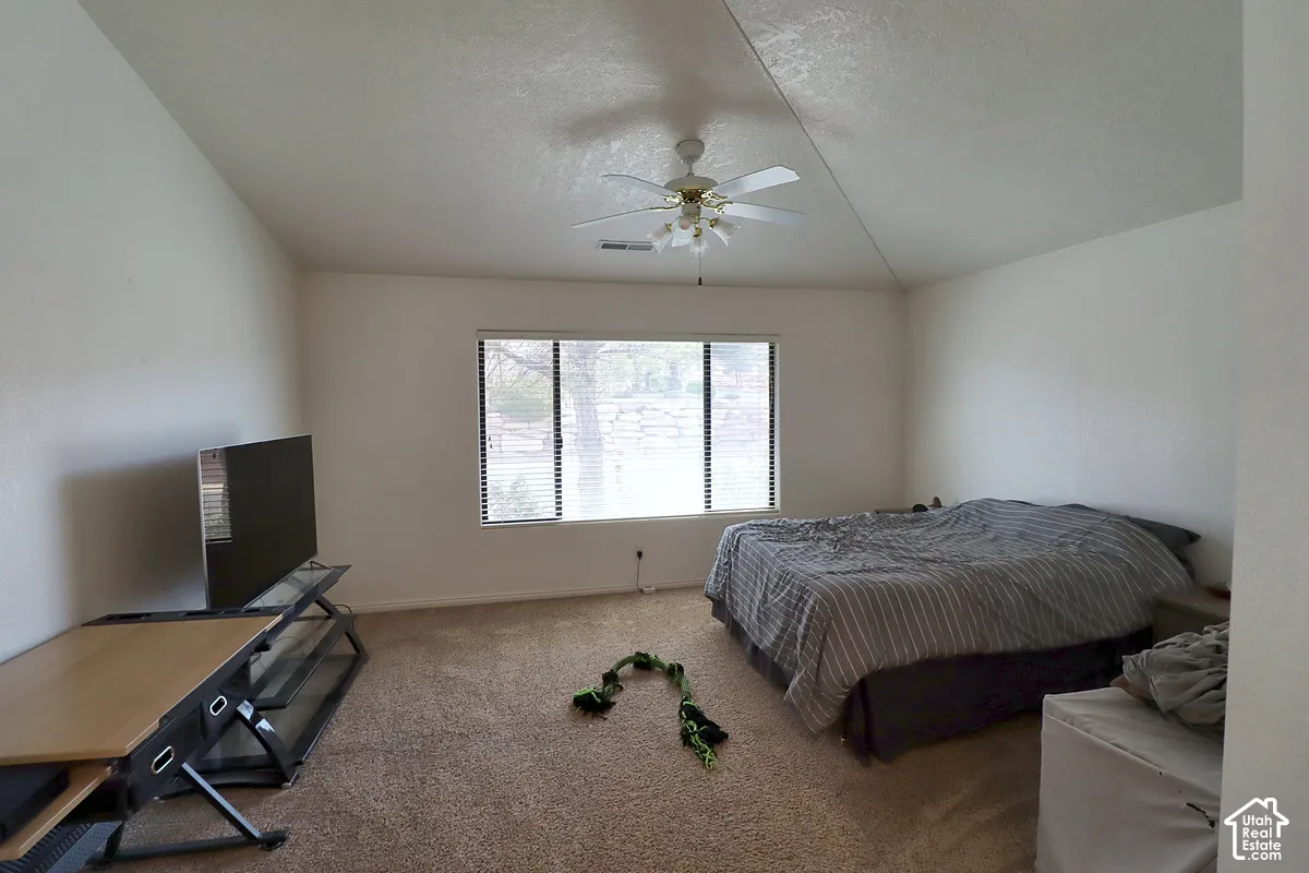 Vaulted ceiling featuring a ceiling fan with integrated lighting, window with blinds, and neutral tone carpet flooring