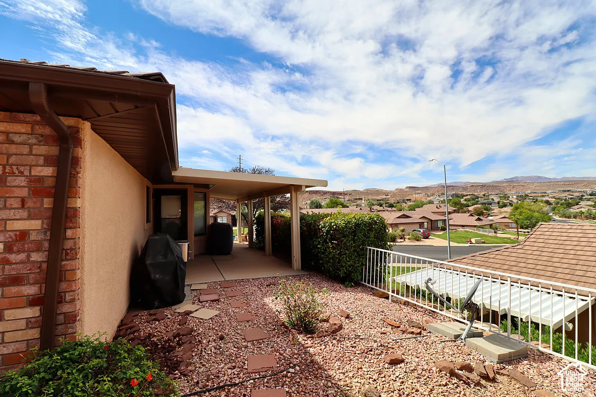 Brick and stucco exterior with a covered patio, concrete paving, and a white metal railing