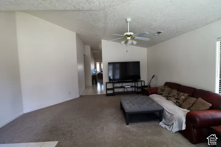 Carpeted living area with a ceiling fan light fixture and window with blinds