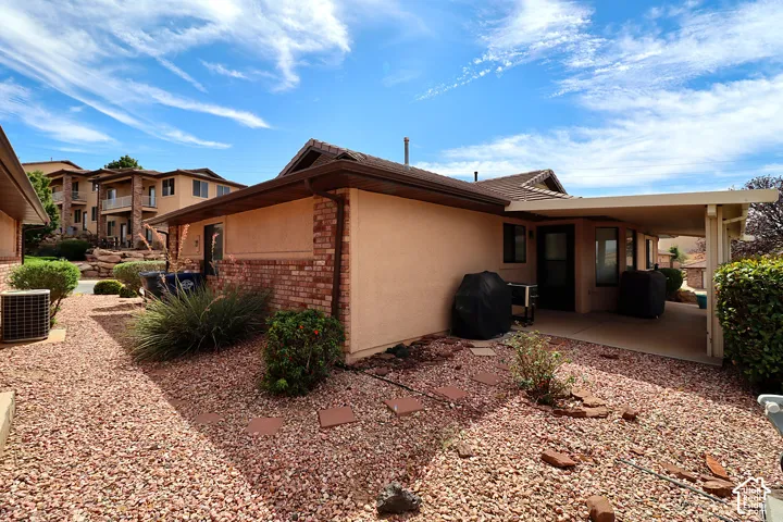 Rear exterior with covered patio, stucco siding, brick detailing, and a gravel landscape