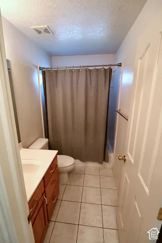White tile flooring, wood-finish vanity with white countertop, and a white toilet