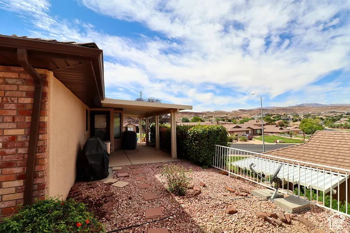 Brick and stucco exterior with a covered patio, concrete paving, and a white metal railing