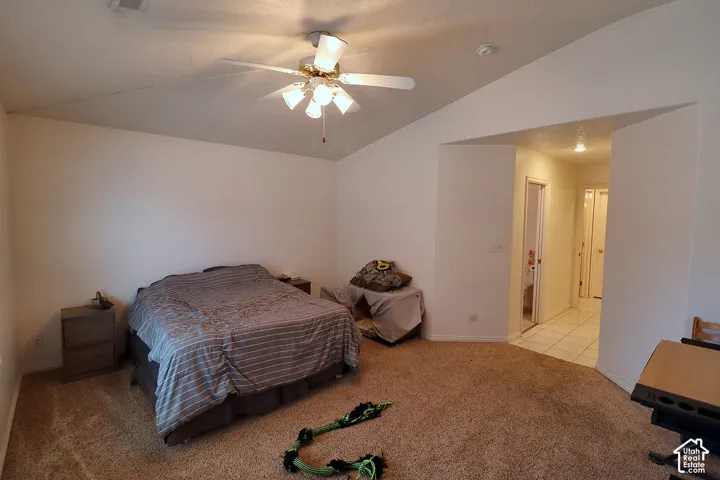 Vaulted ceiling with a ceiling fan, plush carpeting, and an arched doorway leading to a tiled hallway