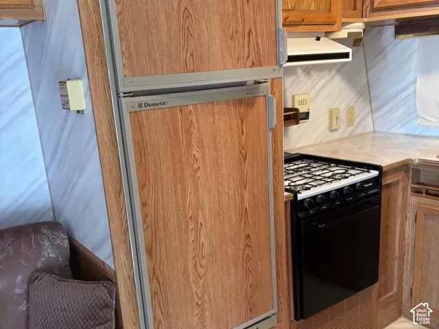 Built-in refrigerator with wood-finish paneling, full-size gas range, solid surface countertop, and wood-finish cabinetry