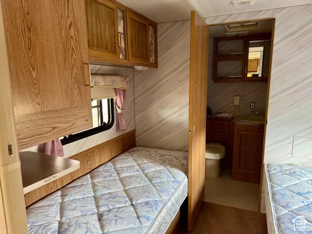 Built-in wood-finish cabinetry, integrated shelving, and a compact bathroom featuring a sink and toilet