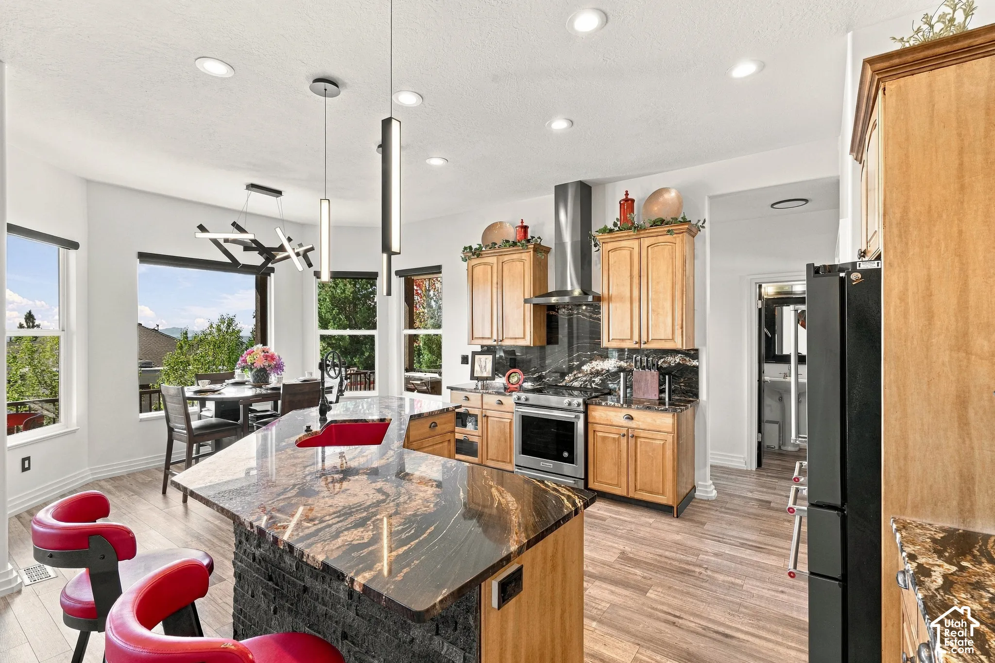 Open-concept kitchen and dining area featuring wood-finish cabinetry, a large center island with stone countertop, stainless steel appliances, and pendant lighting