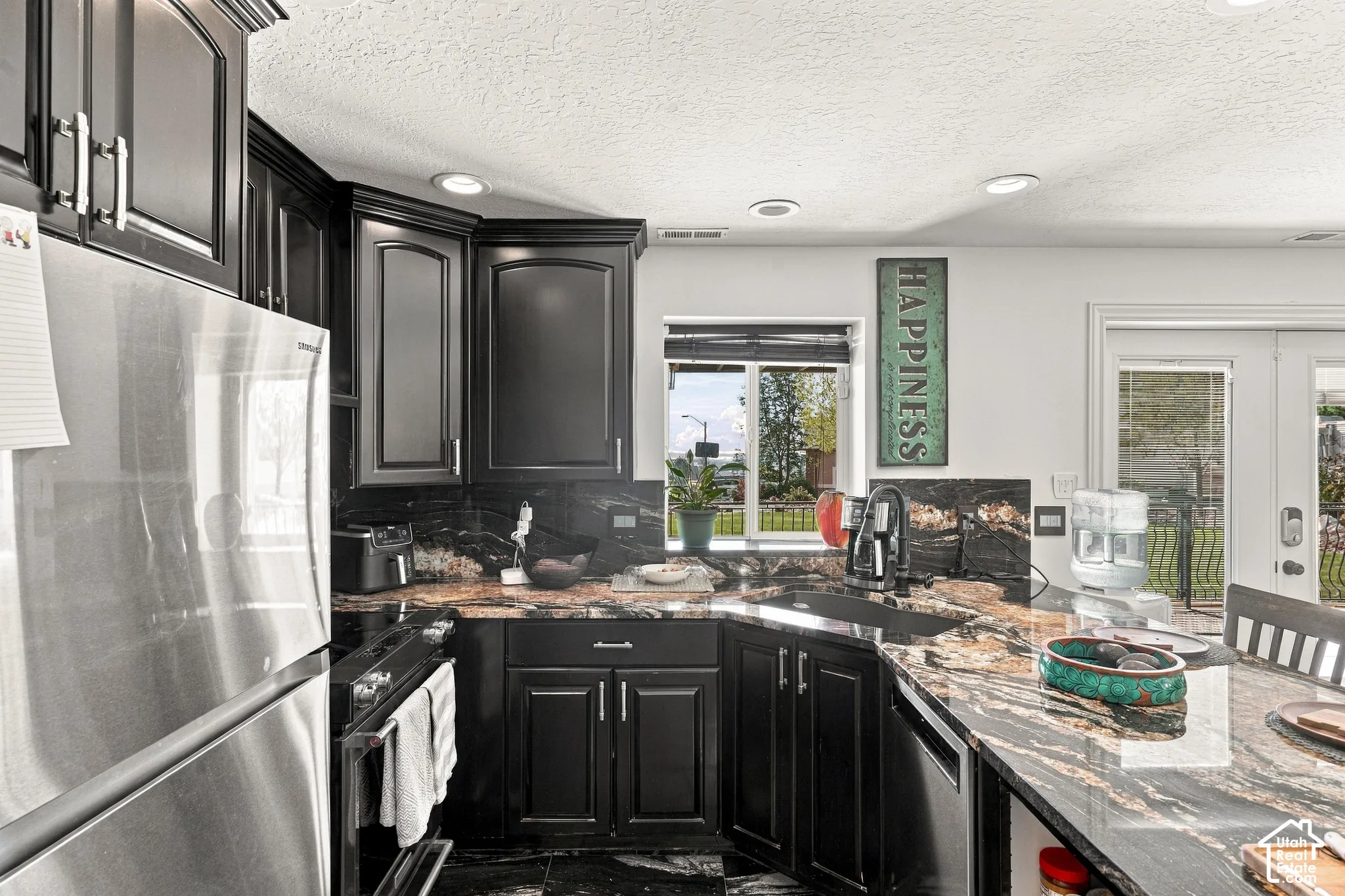 Corner kitchen with dark cabinetry, stone countertops, stainless steel appliances, and recessed lighting