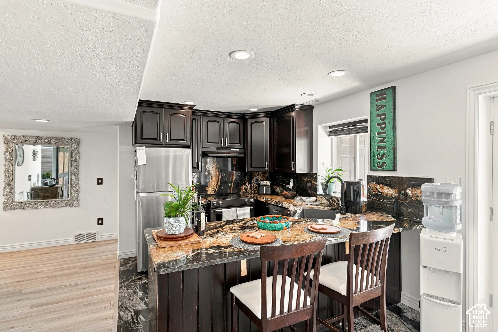 Kitchen featuring dark wood cabinetry, stainless steel appliances, and a multi-toned stone countertop with an integrated breakfast bar