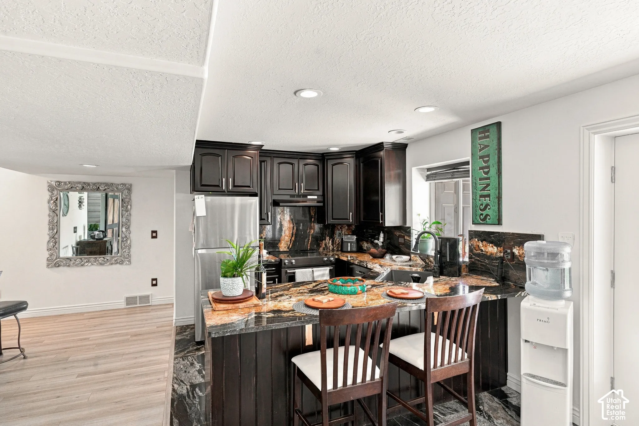 Kitchen featuring dark wood cabinetry, stainless steel refrigerator, dark stone countertops, and recessed lighting