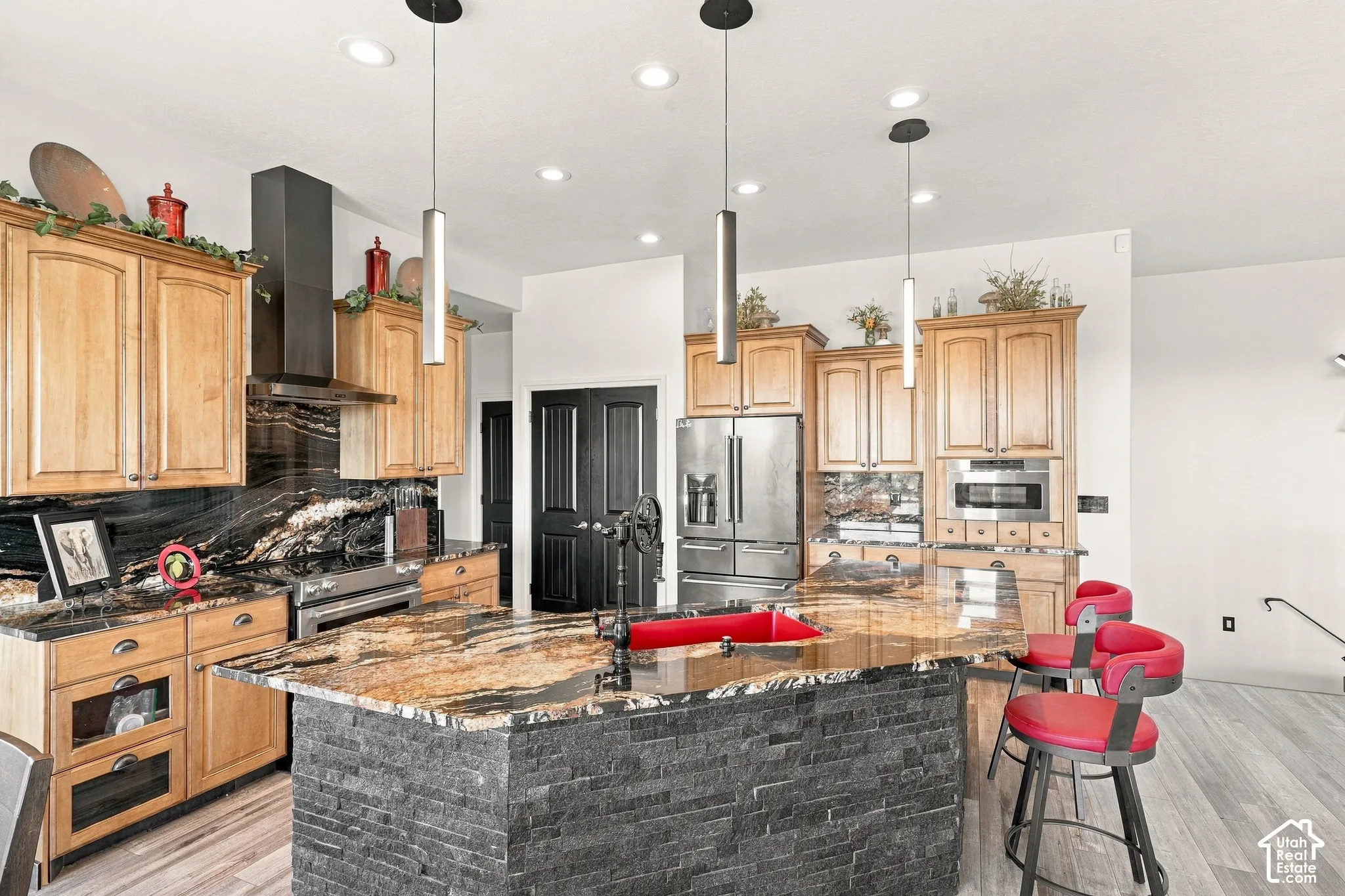 Gourmet kitchen featuring a large island with a stone-clad base, integrated stainless steel appliances, custom wood cabinetry, and pendant lighting