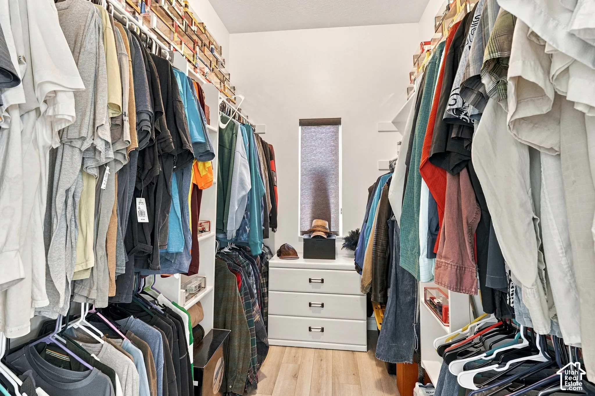 Walk-in closet featuring built-in shelving, hanging rods, central drawer unit, and wood-finish flooring