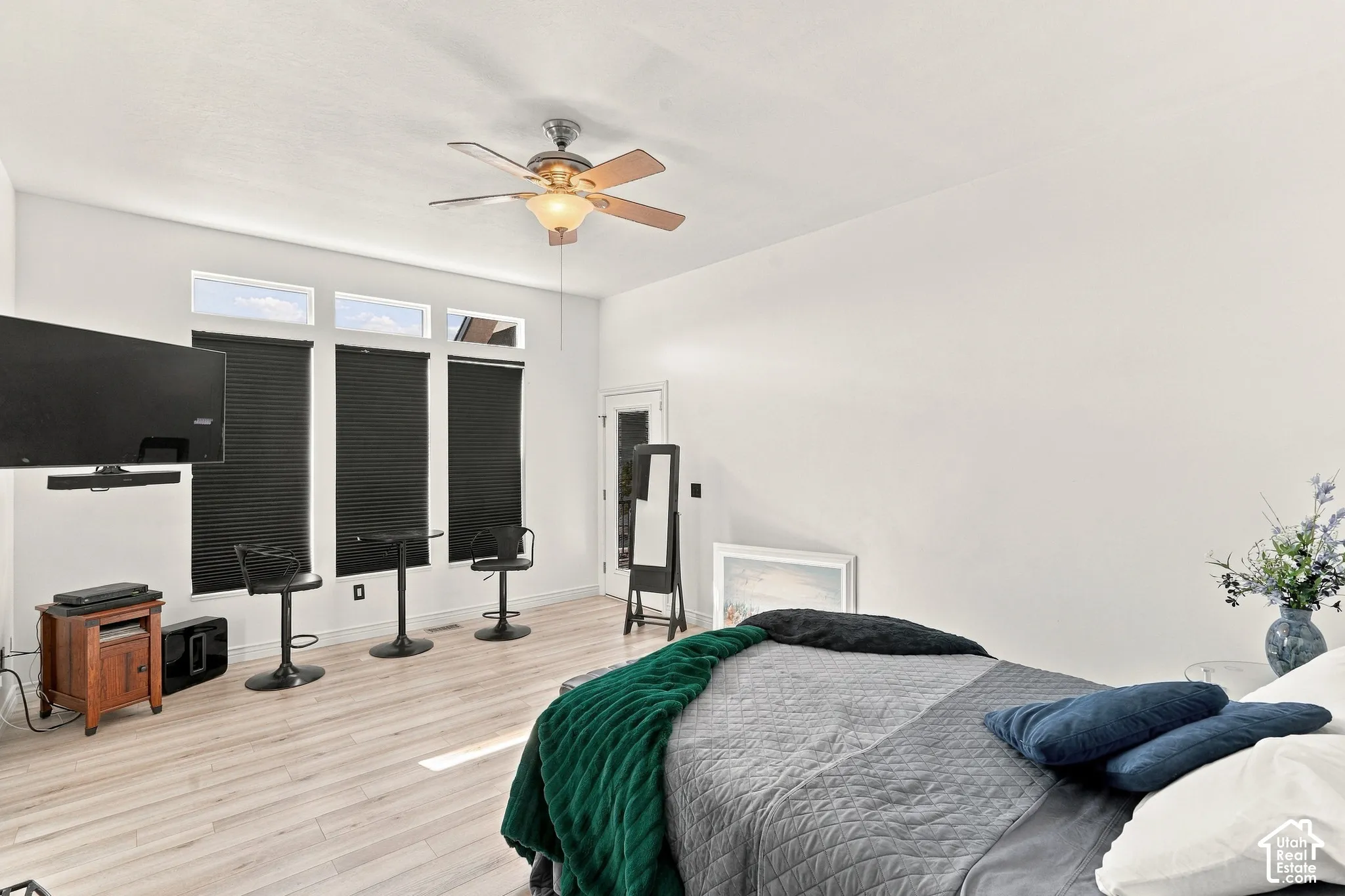 Wood-finish flooring, ceiling fan with integrated lighting, multiple windows with blinds, and white painted walls