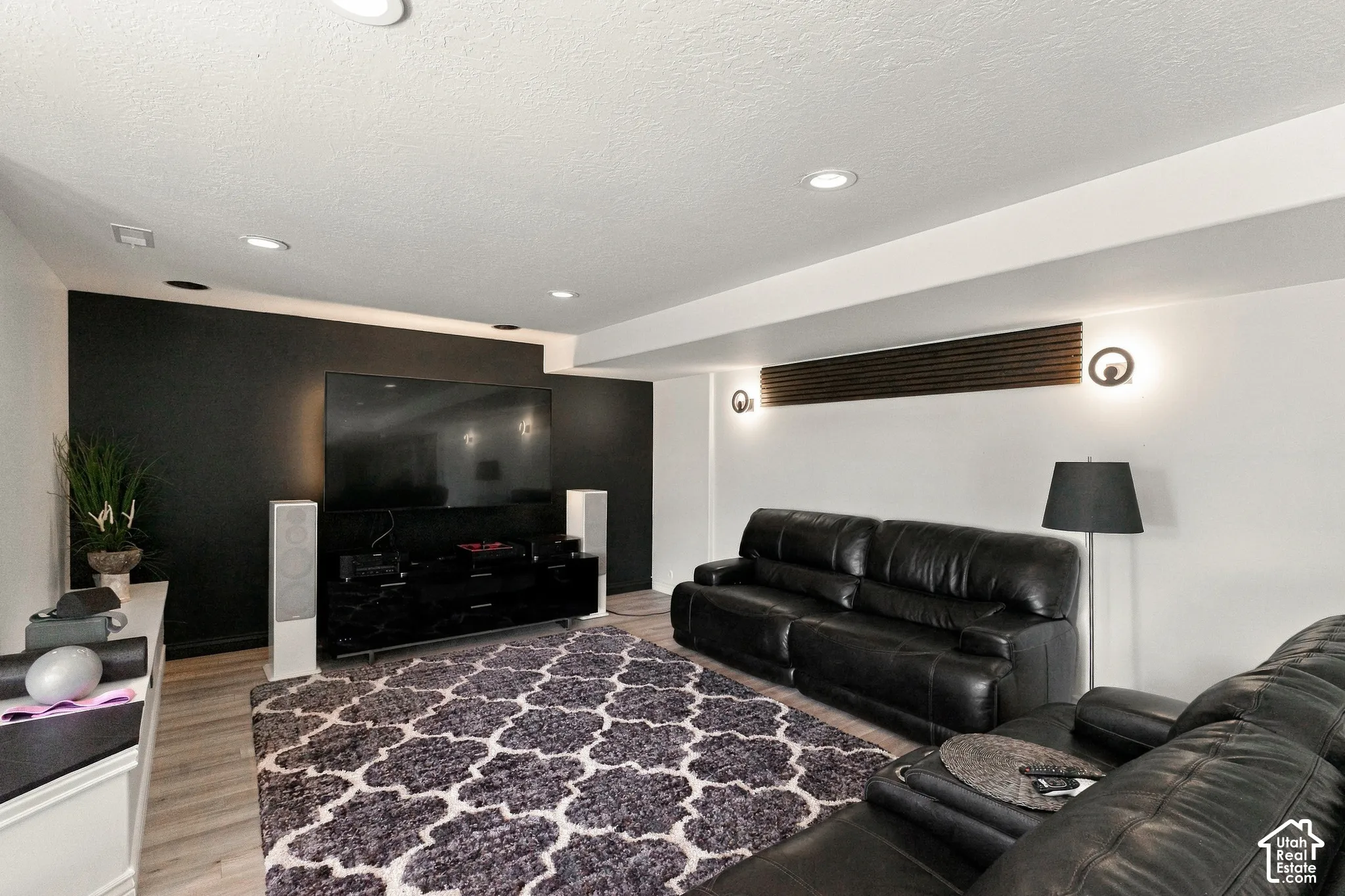 Recessed lighting, wood-finish flooring, accent wall, modern wall sconces, and overhead beam with integrated lighting