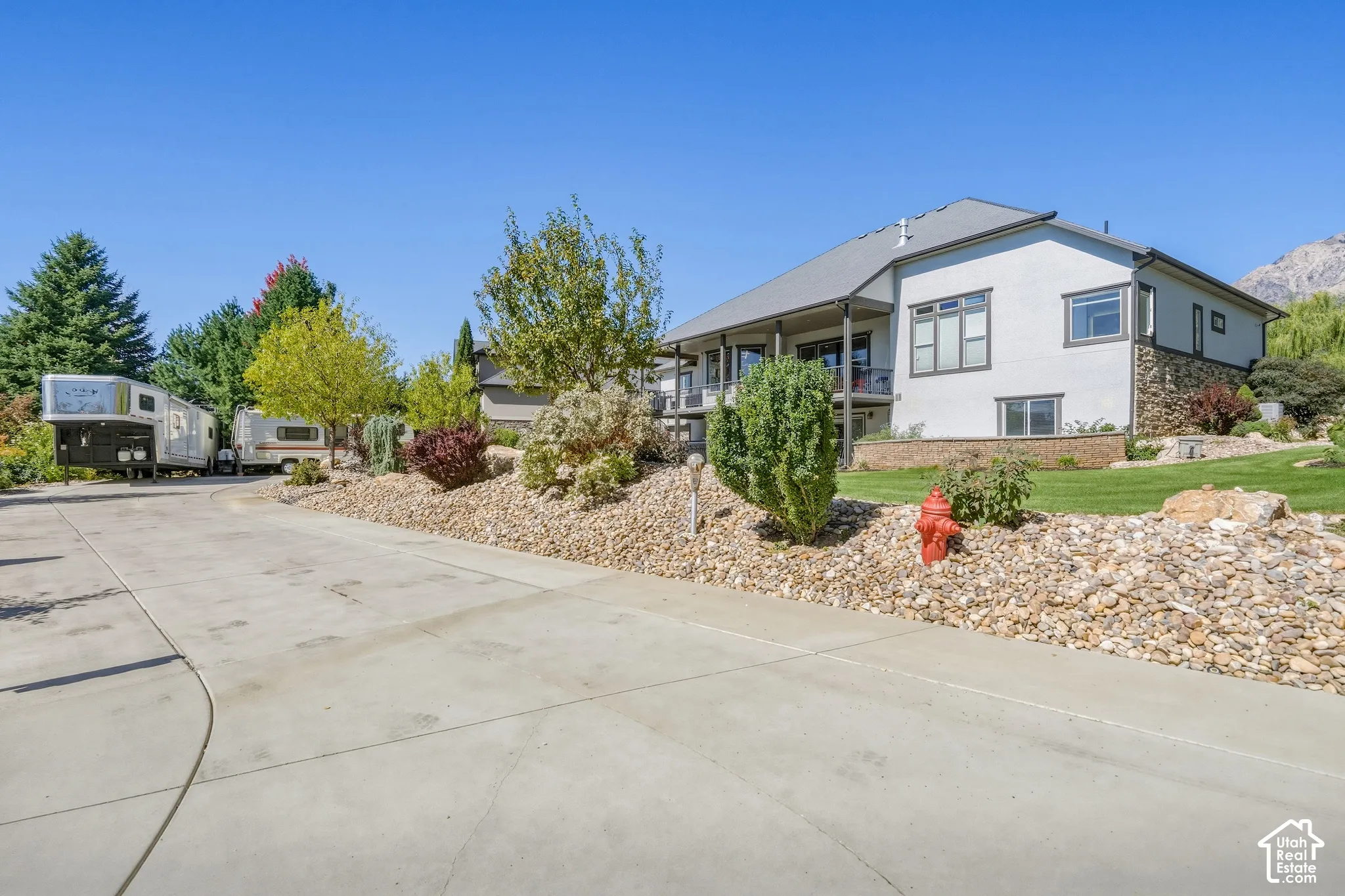 Spacious residence with a concrete driveway and circular turnaround, mature landscaping featuring evergreen and deciduous trees, drought-resistant rock hardscaping, and a covered front porch entry