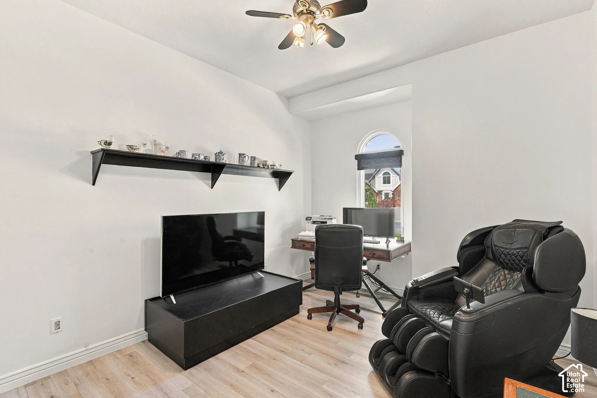 Light wood-finish flooring, a ceiling fan with integrated lighting, and an arched window with a roller shade