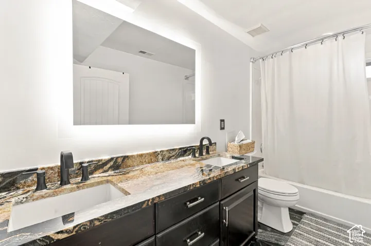 Double vanity with integrated sinks, back-lit mirror, dark wood-finish cabinetry with silver-tone hardware, and a stone countertop