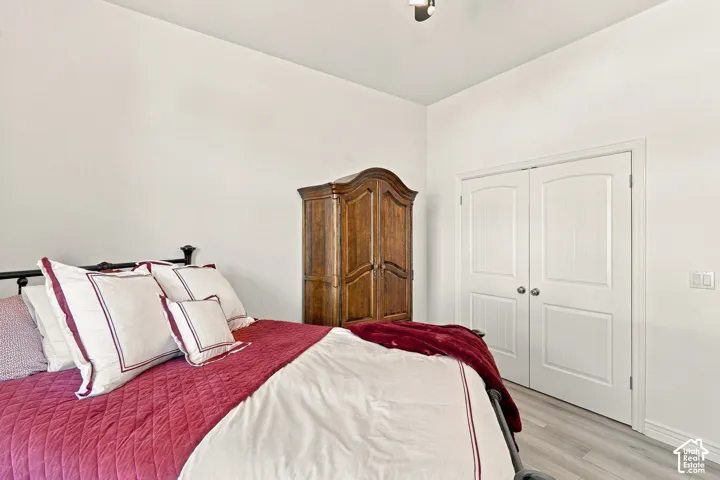 Serene bedroom featuring a wood-finish armoire, plush bedding in jewel tones, decorative throw pillows, wood-finish flooring, and dual closet doors with white six-panel styling