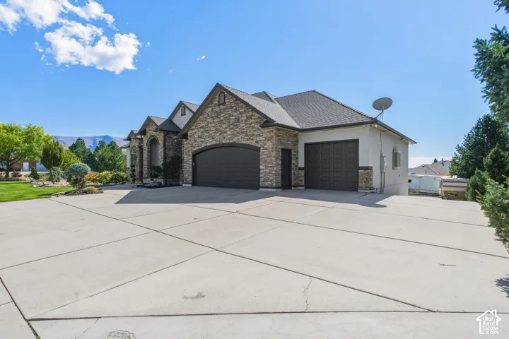 Expansive concrete driveway, stone and stucco exterior, arched garage doors, and landscaped surroundings