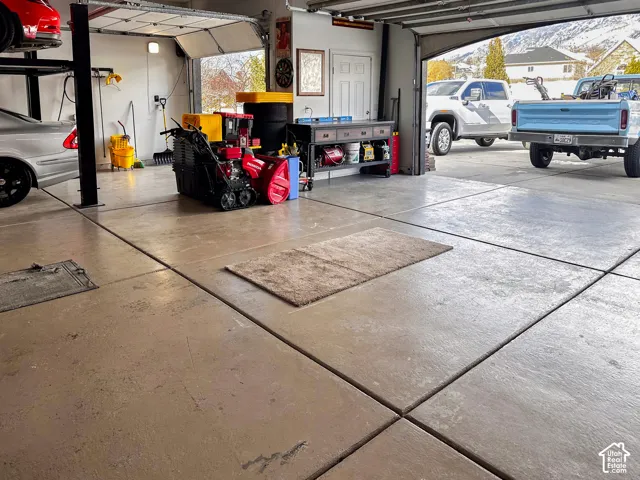 Spacious three-car garage featuring polished concrete flooring with control joints, overhead garage doors with natural light, wall-mounted storage systems, and direct driveway access