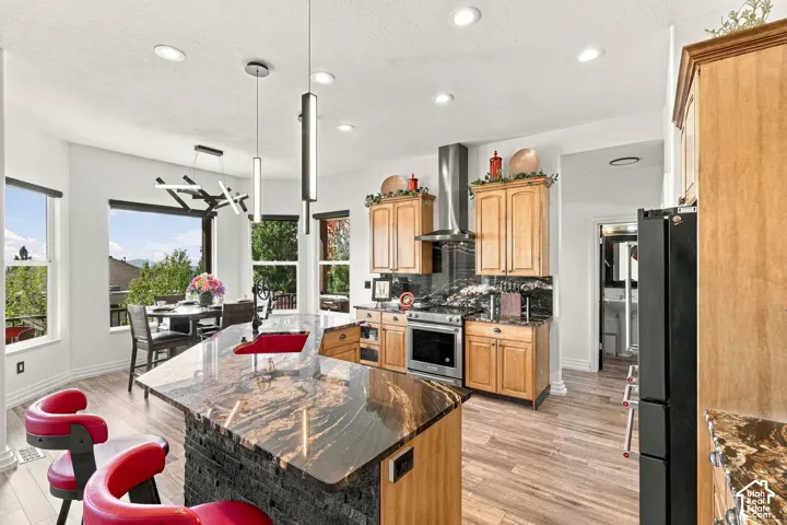 Open-concept kitchen and dining area featuring wood-finish cabinetry, a large center island with stone countertop, stainless steel appliances, and pendant lighting