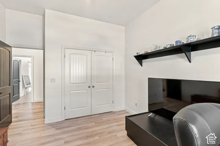 Bright bedroom featuring gleaming wood-finish flooring, white double-panel closet doors with hardware, and a black floating shelf