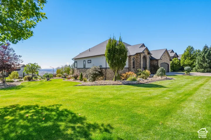 Expansive manicured lawn with professional striping and mature landscaping, anchored by a substantial stone and siding residence featuring peaked rooflines and multiple architectural elevations