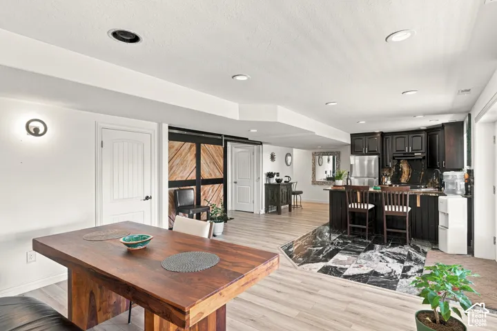 Recessed ceiling lighting, wood-finish flooring, dark wood cabinetry, black and white marble-look flooring, and a barn door with a wood panel design