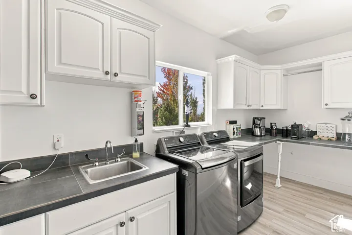 White cabinetry, utility sink, dark countertops, and wood-finish flooring