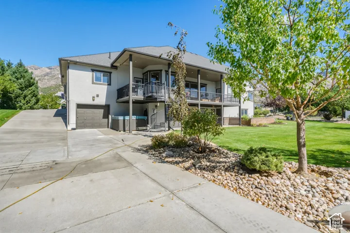 Stucco exterior with a two-car garage, upper and lower balconies, and a hot tub