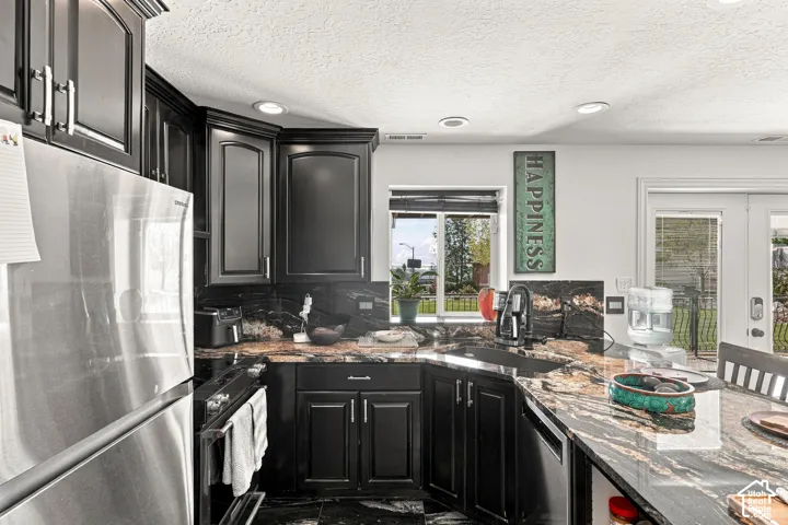 Corner kitchen with dark cabinetry, stone countertops, stainless steel appliances, and recessed lighting
