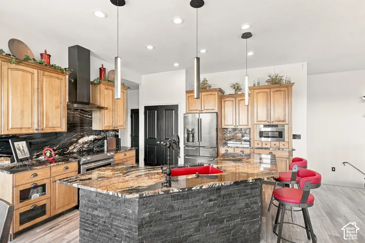 Gourmet kitchen featuring a large island with a stone-clad base, integrated stainless steel appliances, custom wood cabinetry, and pendant lighting