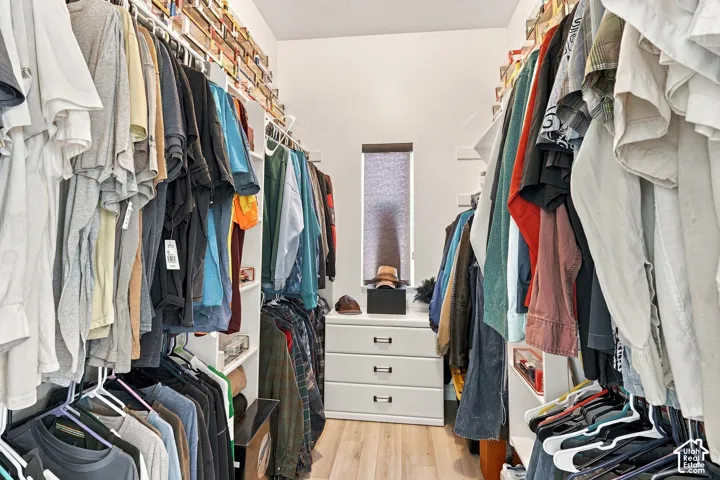 Walk-in closet featuring built-in shelving, hanging rods, central drawer unit, and wood-finish flooring