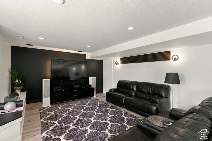 Recessed lighting, wood-finish flooring, accent wall, modern wall sconces, and overhead beam with integrated lighting