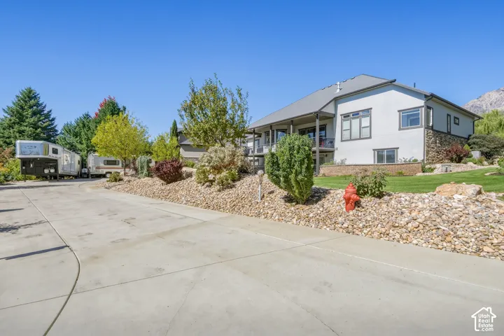 Spacious residence with a concrete driveway and circular turnaround, mature landscaping featuring evergreen and deciduous trees, drought-resistant rock hardscaping, and a covered front porch entry