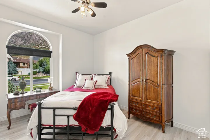 Charming bedroom featuring a large arched window with wood-finish sill, wood-finish flooring throughout, a ceiling fan with integrated lighting, and a traditional wood-finish wardrobe with arched detailing
